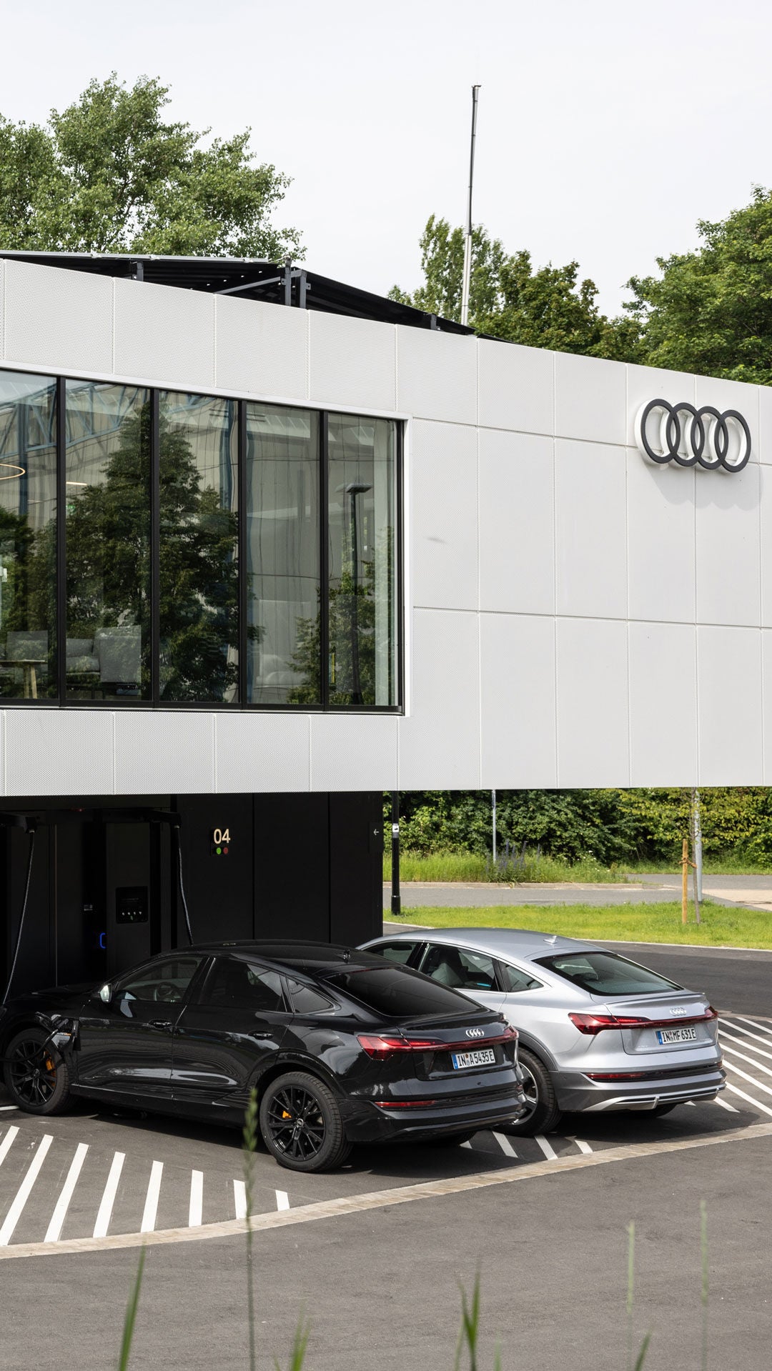 Zwei Etagen des Audi charging hub Nürnbergs mit mehreren E-Autos an Ladepunkten und einer Lounge im Obergeschoss.