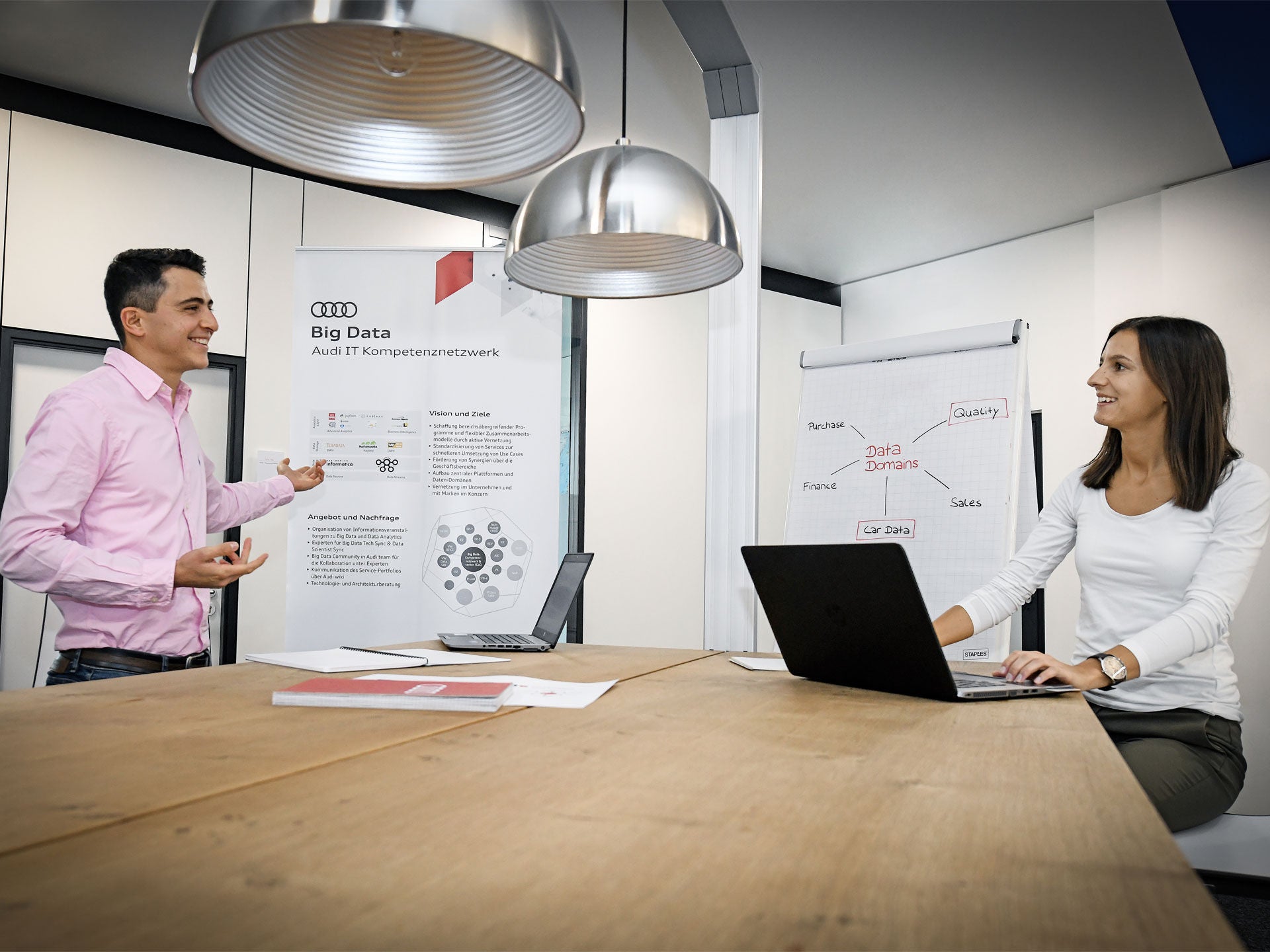 Two people discussing in an office with laptops on a wooden table