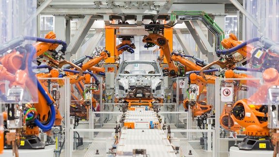 Automatisierte Montagelinie mit orangen KUKA-Robotern beim Bau einer Audi-Karosserie.