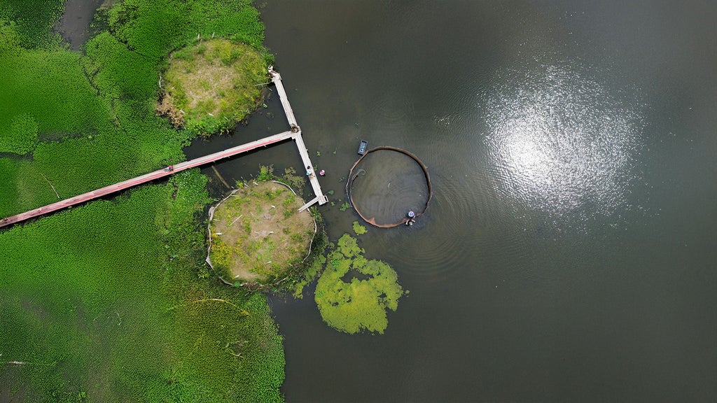 Aerial view of two planted water islands and a third under construction, connected by a dock.