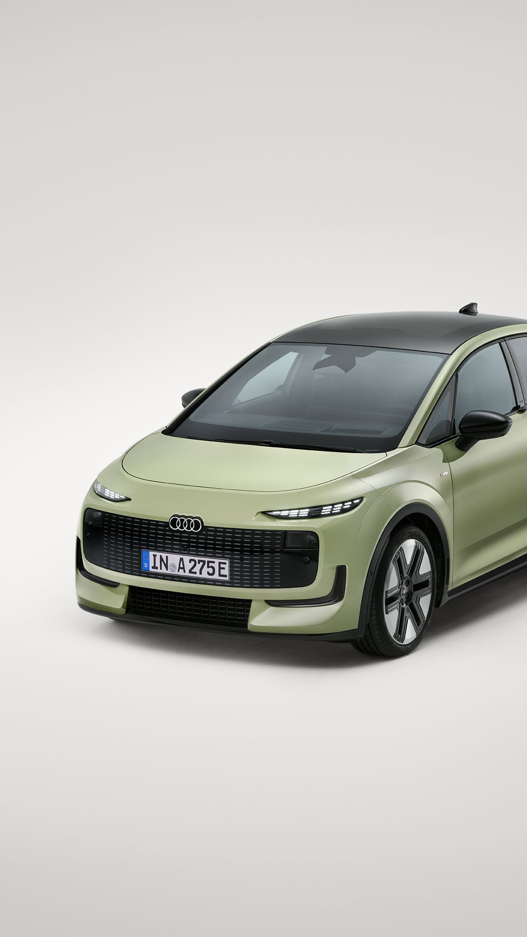Audi A2 e-tron vert clair, vue de trois quarts depuis l'avant sur fond clair. Ce véhicule électrique est doté d'un toit noir, de phares LED étroits et d'une face avant fermée au design marquant.