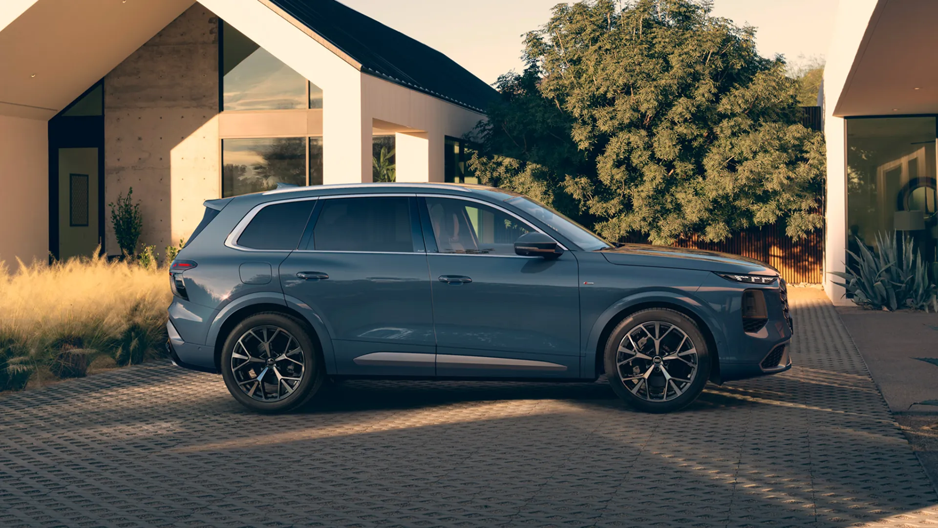 Grey Audi Q7 SUV facing front, parked on tarmac in front of building with patterned facade.