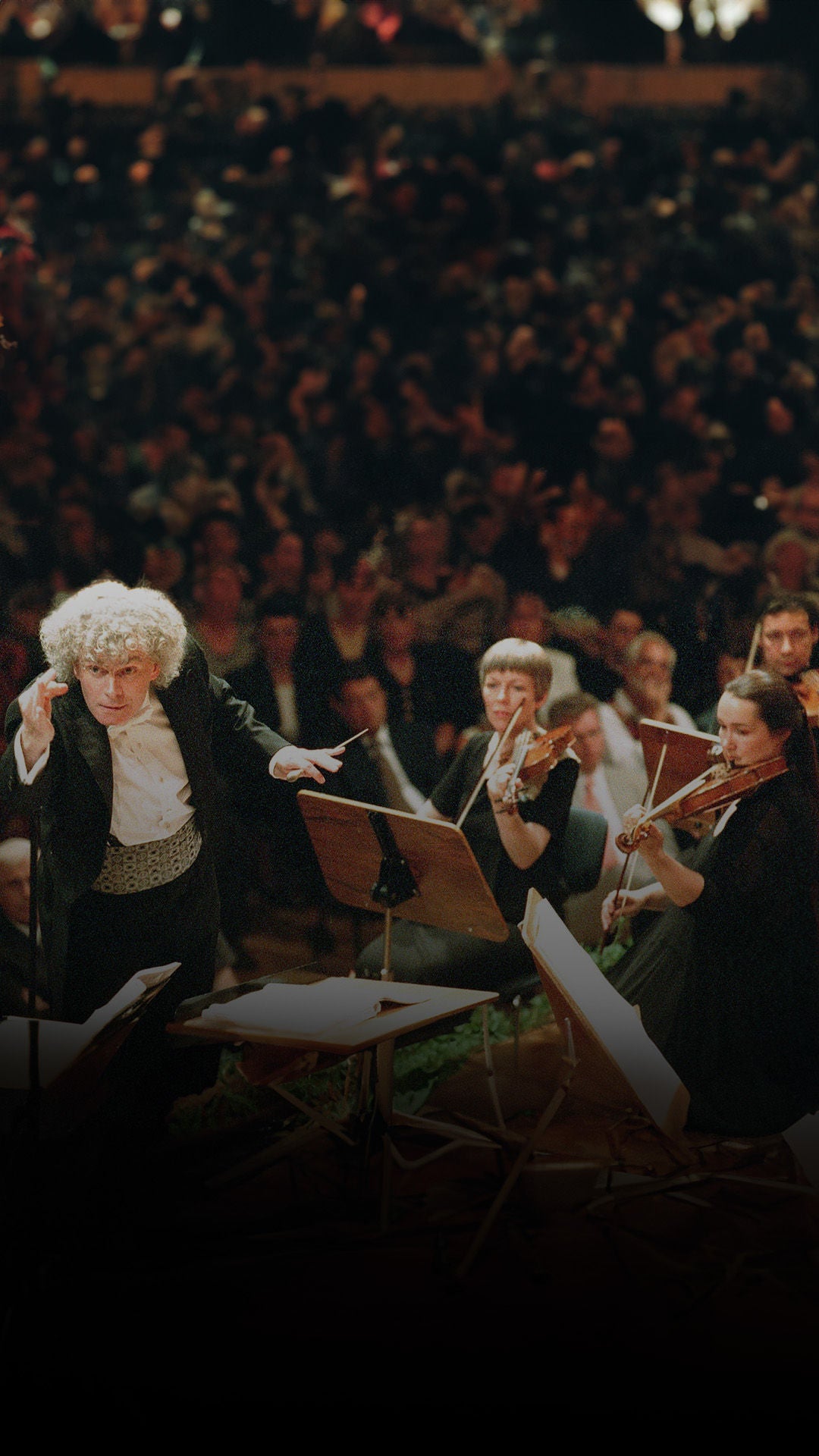 Dirigent mit grauen, lockigen Haaren und weiteren Musikern.