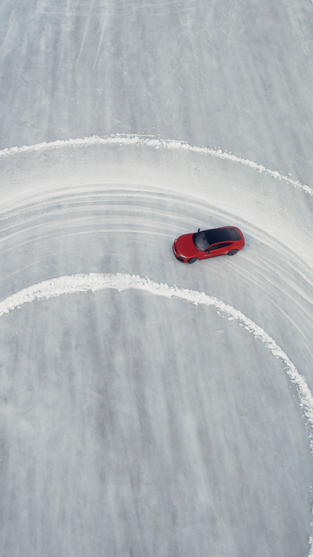 Red Audi RS e-tron GT performance takes a large curve on an icy surface, photographed from the air.