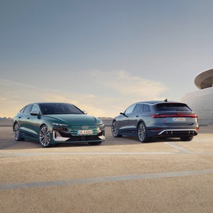 Two sleek Audi cars parked on a modern concrete surface with a serene sunset backdrop. The green sedan and grey SUV evoke elegance and innovation.