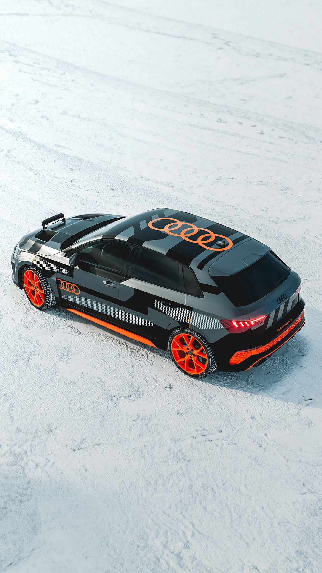 Black-orange foiled Audi RS 3 driving experience with eye-catching wheel design stands on a snow-covered surface, photographed from above.