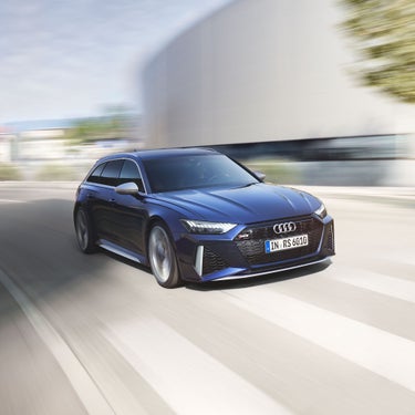 Dunkelblauer Audi RS 6 Avant fährt dynamisch durch städtische Umgebung, leichte Bewegungsunschärfe.