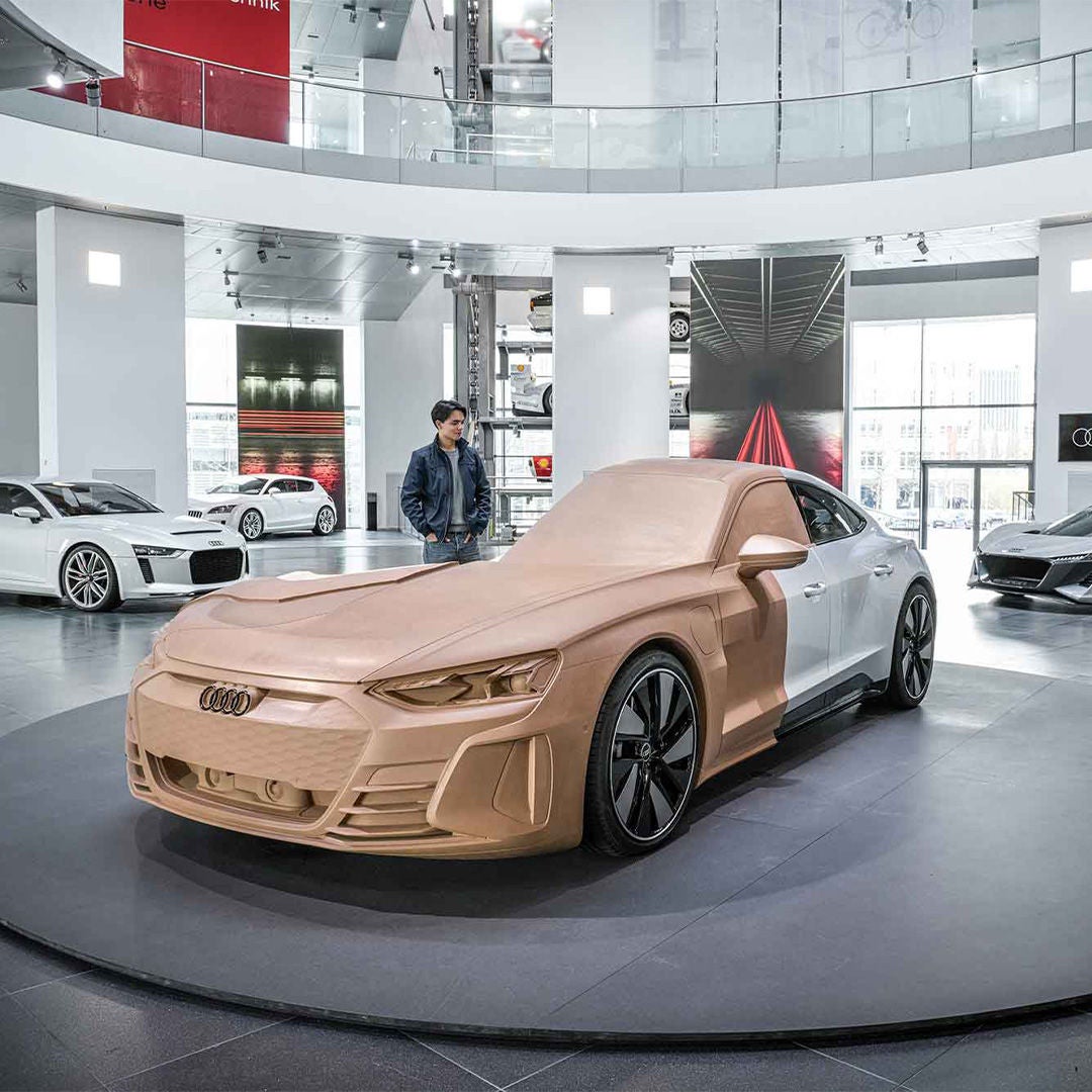 Audi in heller Ausstellungshalle; dahinter steht ein junger Mann, weitere Fahrzeuge im Hintergrund.