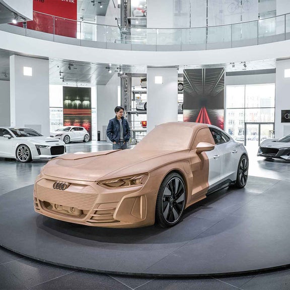 Tonmodell eines Audi in Ausstellungshalle, Junge daneben; umgeben von Serienfahrzeugen.