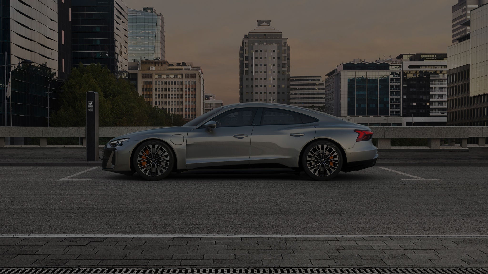 Electric Audi car charging at a station in urban parking area at dusk.
