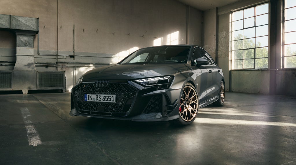 Das Sondermodell RS 3 competition limited mit Rädern in Neodymgold und Heckdiffusor von schräg vorn in einer Werkstatthalle stehend.