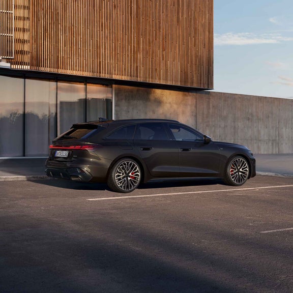 Ein schwarzer Audi A5 Avant e-hybrid in der Seitenansicht vor einer grauen Beton Wand mit großen Fenstern.