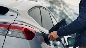A hand plugs a charging cable into the electric vehicle's port, showcasing modern charging infrastructure and a sleek car design.
