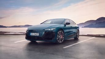 Teal-coloured Audi S6 Sportback e-tron facing left, parked on tarmac with body of water and mountains behind.