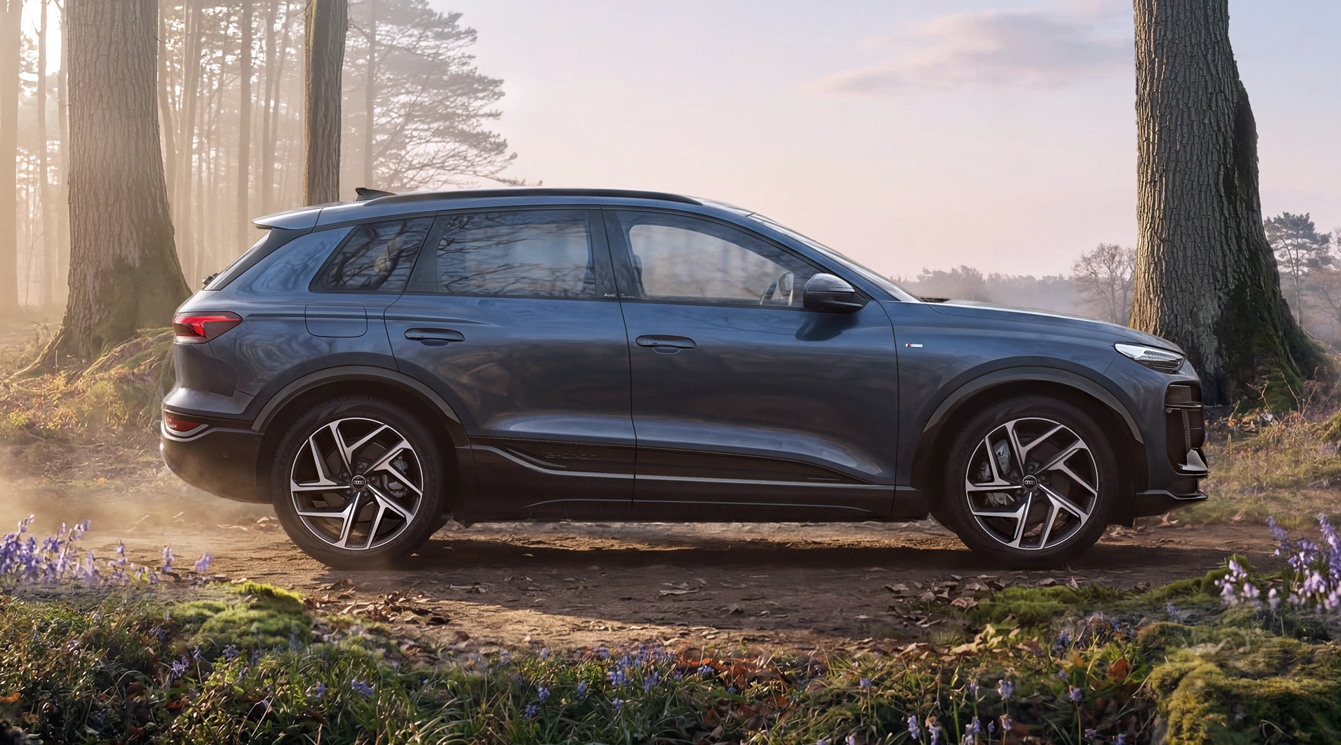 The dark blue Q6 SUV e-tron is shown in profile in front of an urban building. In the foreground, slightly to the side of the car, stands a young, fashionable woman.