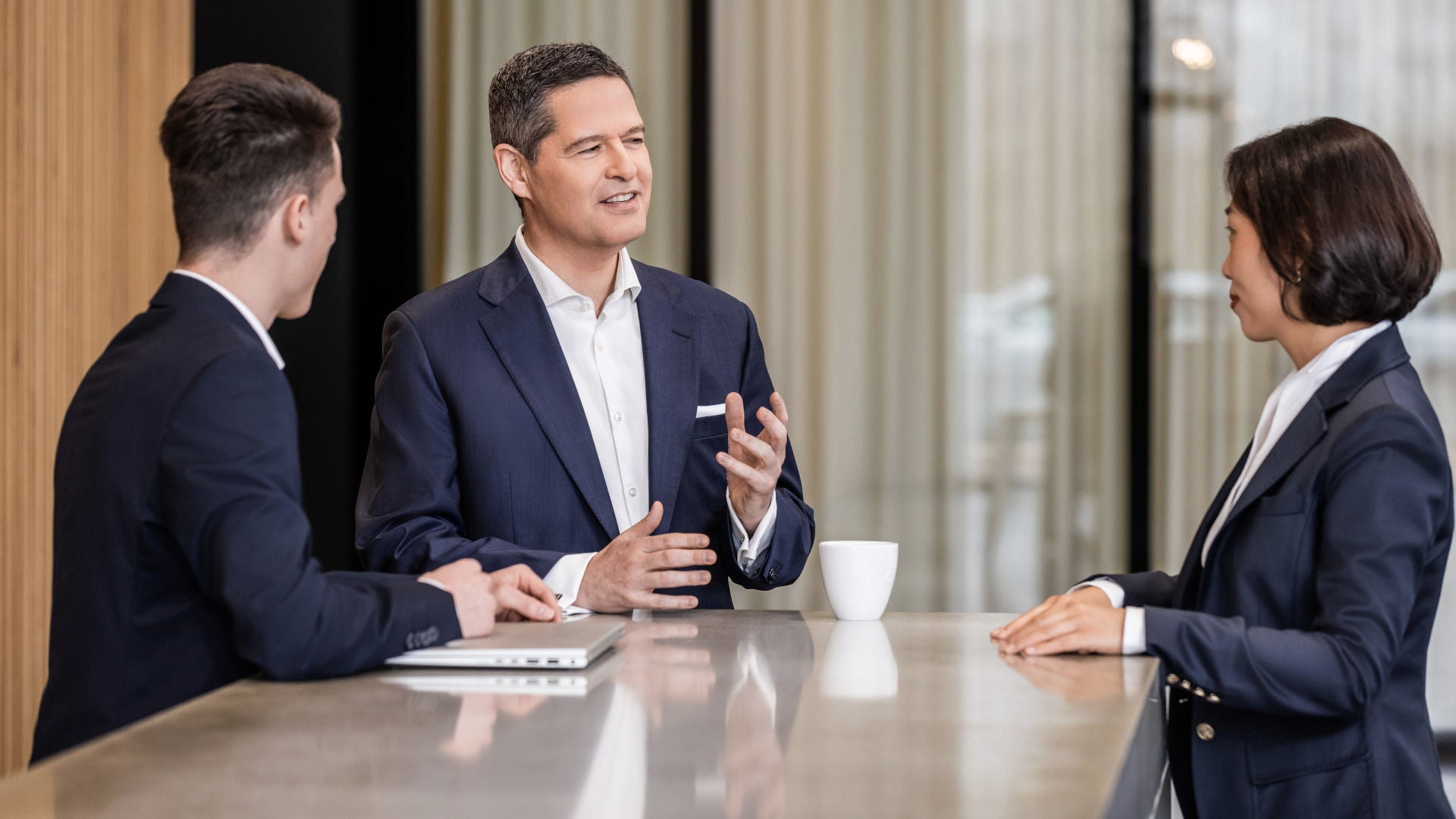 Xavier Ross steht mit zwei Personen an einem Tisch und sie reden miteinander