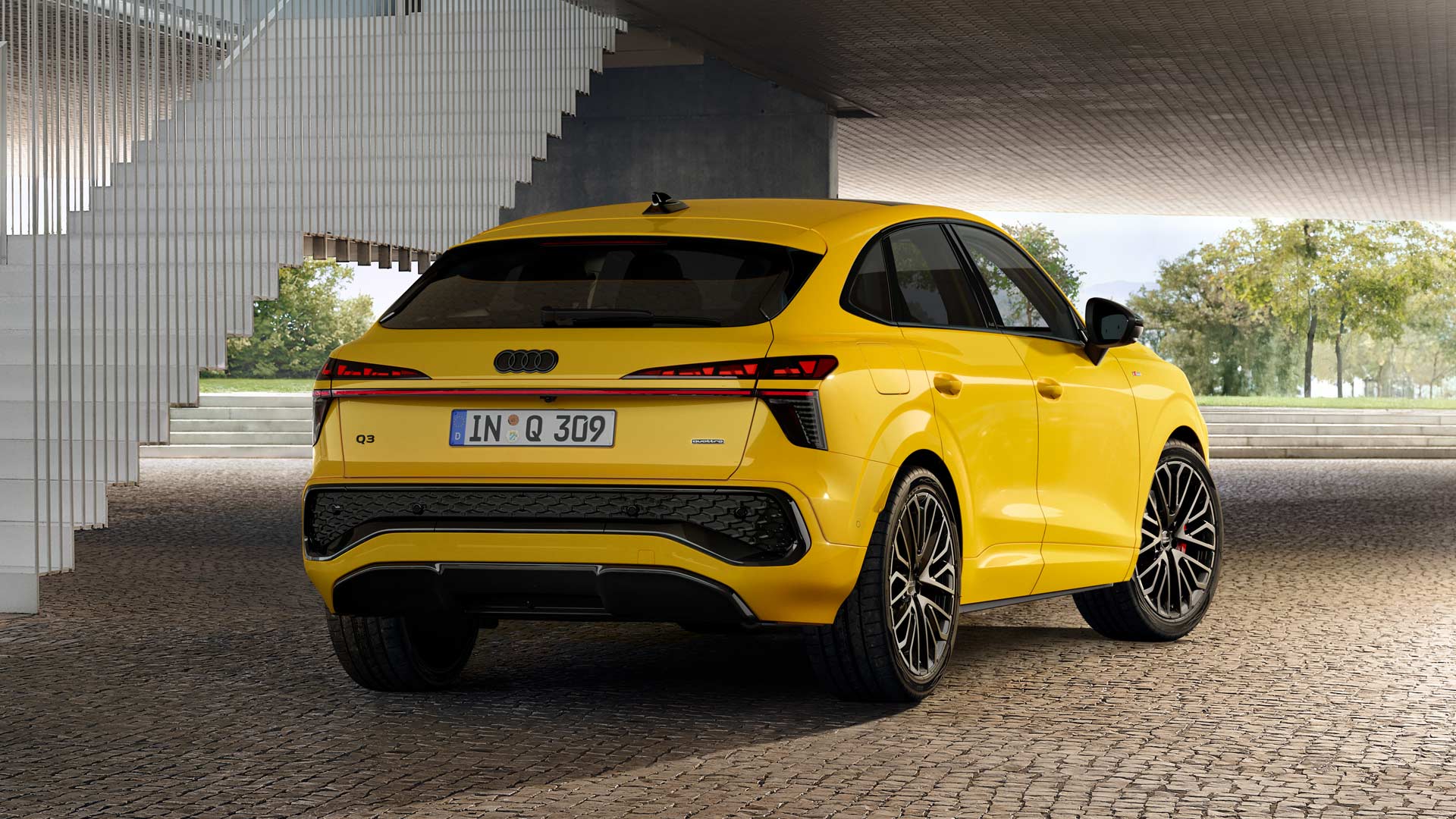 A yellow Q3 Sportback is parked on a paved surface in front of a stair railing.