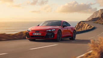 Der e-tron GT quattro fährt bei Sonnenuntergang über eine kurvige Straße entlang einer felsigen Küste.&nbsp;