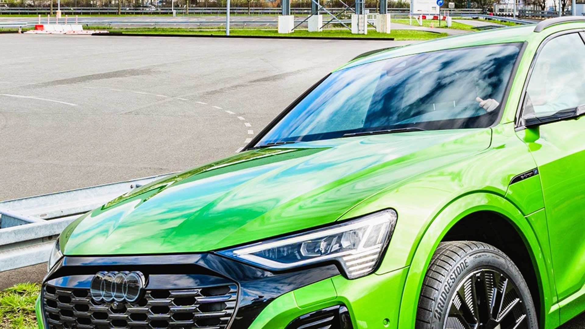 Une Audi Q8 e-tron verte en vue frontale latérale pendant la conduite. On peut voir un circuit de course en arrière-plan.