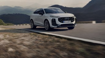 Grey Audi {Model Name} facing front, parked on tarmac in front of building with patterned facade.