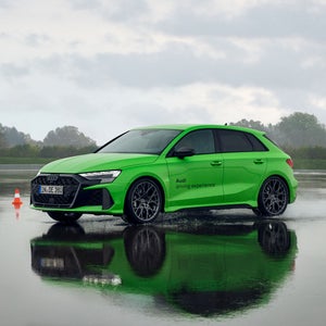 En grön Audi RS 4 på ett vått underlag, med bilens silhuett speglad nedanför den. Till vänster om bilen står en röd och vit trafikkon.