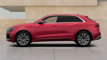 Red Audi Q8 SUV parked by a modern beige wall, viewed from the side with black windows and alloy wheels.