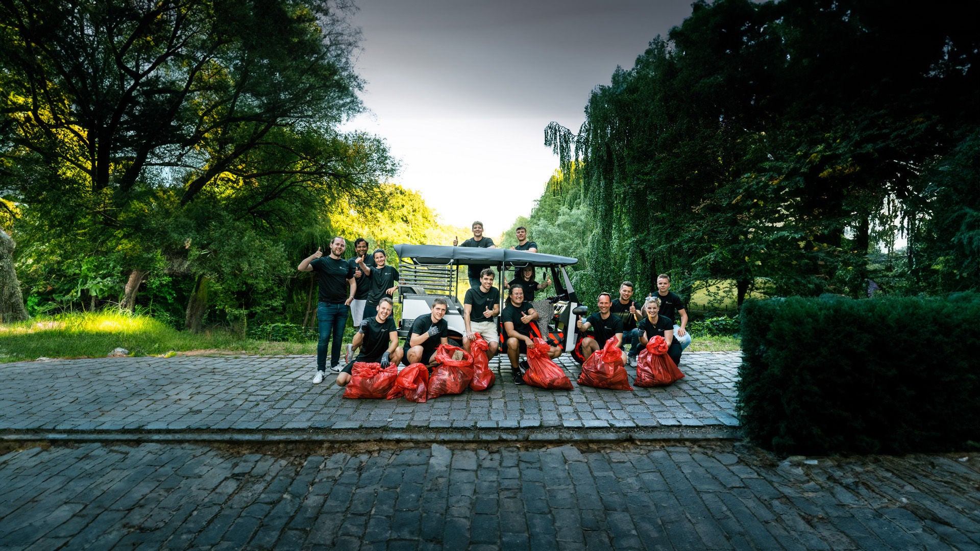 A group of young people stand and squat with filled orange bags next to an e-rickshaw