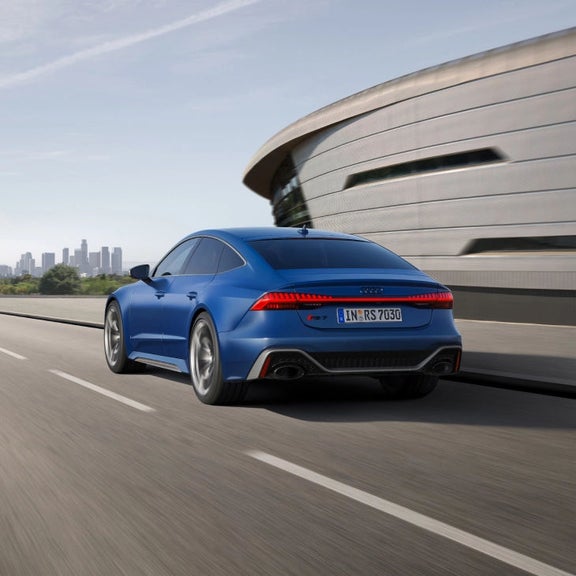 Blue sedan driving on highway with city skyline in background.