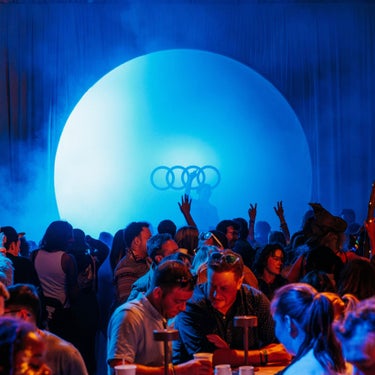 Crowd dancing in front of a dj with Audi logo in the back