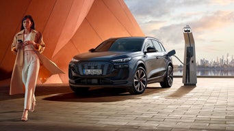 Eine Frau mit Handy in der Hand geht weg von einem SQ6 an einer Ladestation