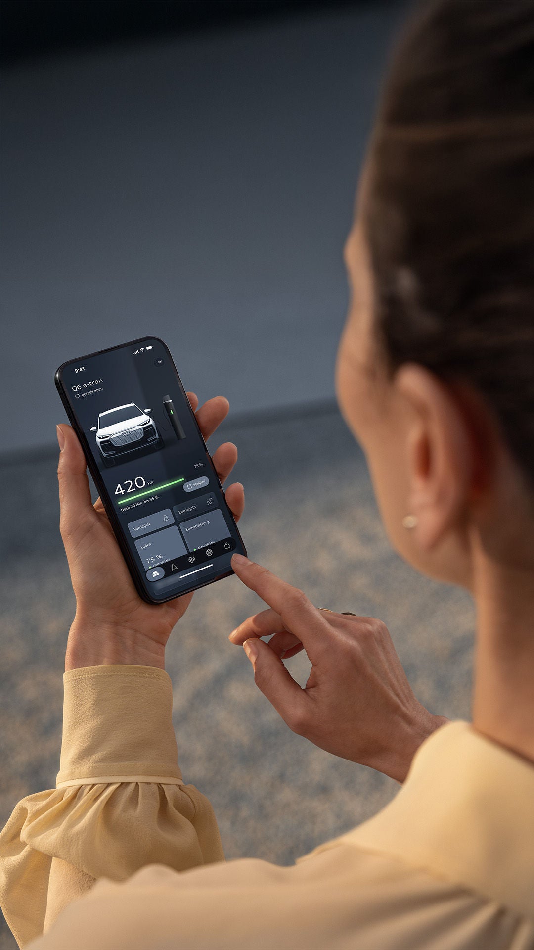 Eine Frau in gelber Bluse beim Überprüfen des Ladestatus ihres Audi A6 e-tron via myAudi App auf ihrem Smartphone.