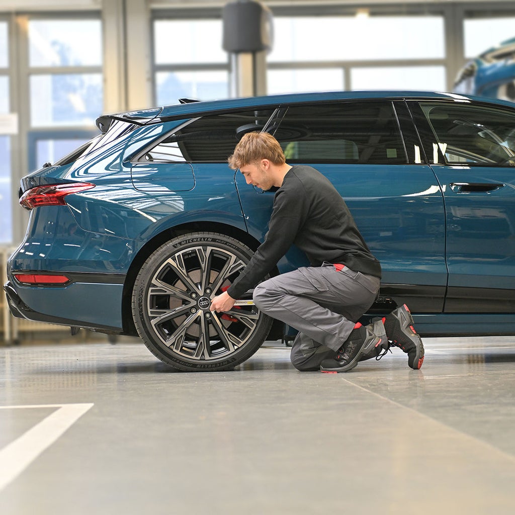 Julian kniet vor einem Hinterreifen eines blauen Audi