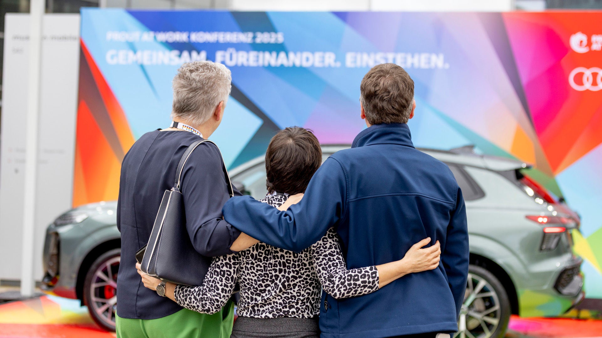 Zusammenstehen für Vielfalt und Chancengleichheit – Mitarbeitende blicken Arm in Arm auf ein Plakat zum Thema Audi Diversity.
