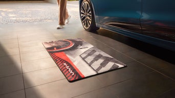 Garagenteppich mit Audi e-tron Design liegt vor blauem Fahrzeug, Person geht vorbei.
