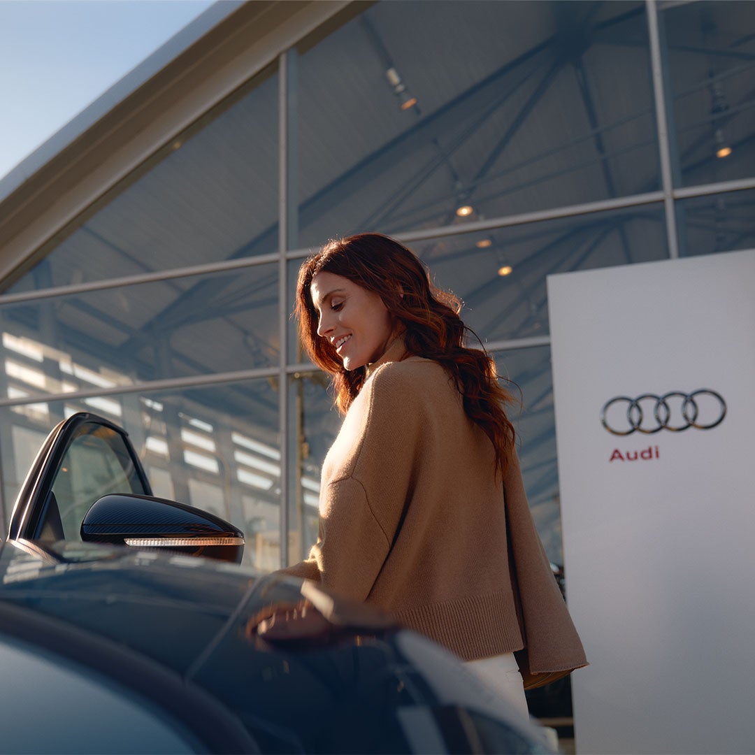 Une femme se trouve devant une concession Audi et souhaite monter dans une voiture.