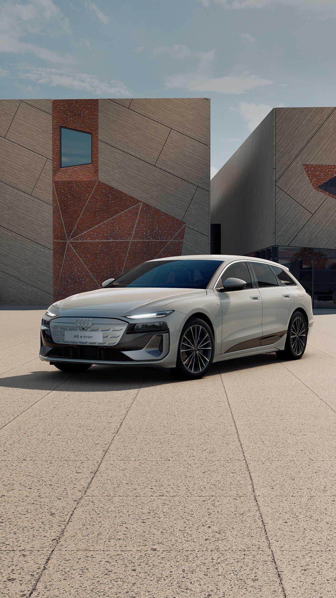 Dreiviertel-/Frontansicht eines beige grauen Audi A6 e-tron vor moderner urbaner Architektur.
