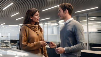 Mann im grauen Pullover übergibt einer Frau einen Autoschlüssel in modernem, hell beleuchtetem Autohaus.