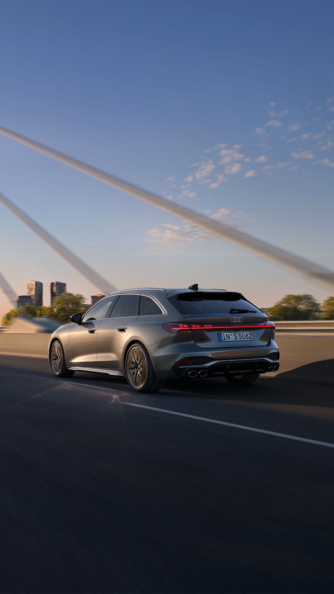 Une audi S5 grise circulant sur un pont au coucher du soleil.