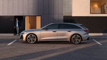 Un Audi A5 Avant couleur champagne est garé devant un bâtiment moderne, tandis qu'une personne sort de l'entrée.