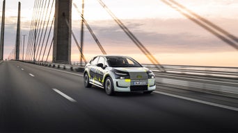 The Audi A2 e-tron with camo livery drives across a bridge