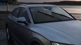 Mann in Audi-Shirt wechselt einen Scheibenwischer an grauem Auto in heller Werkstatt.