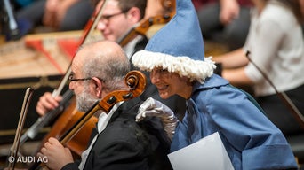 Verkleidete Person schaut einem Cello-Spieler über die Schulter