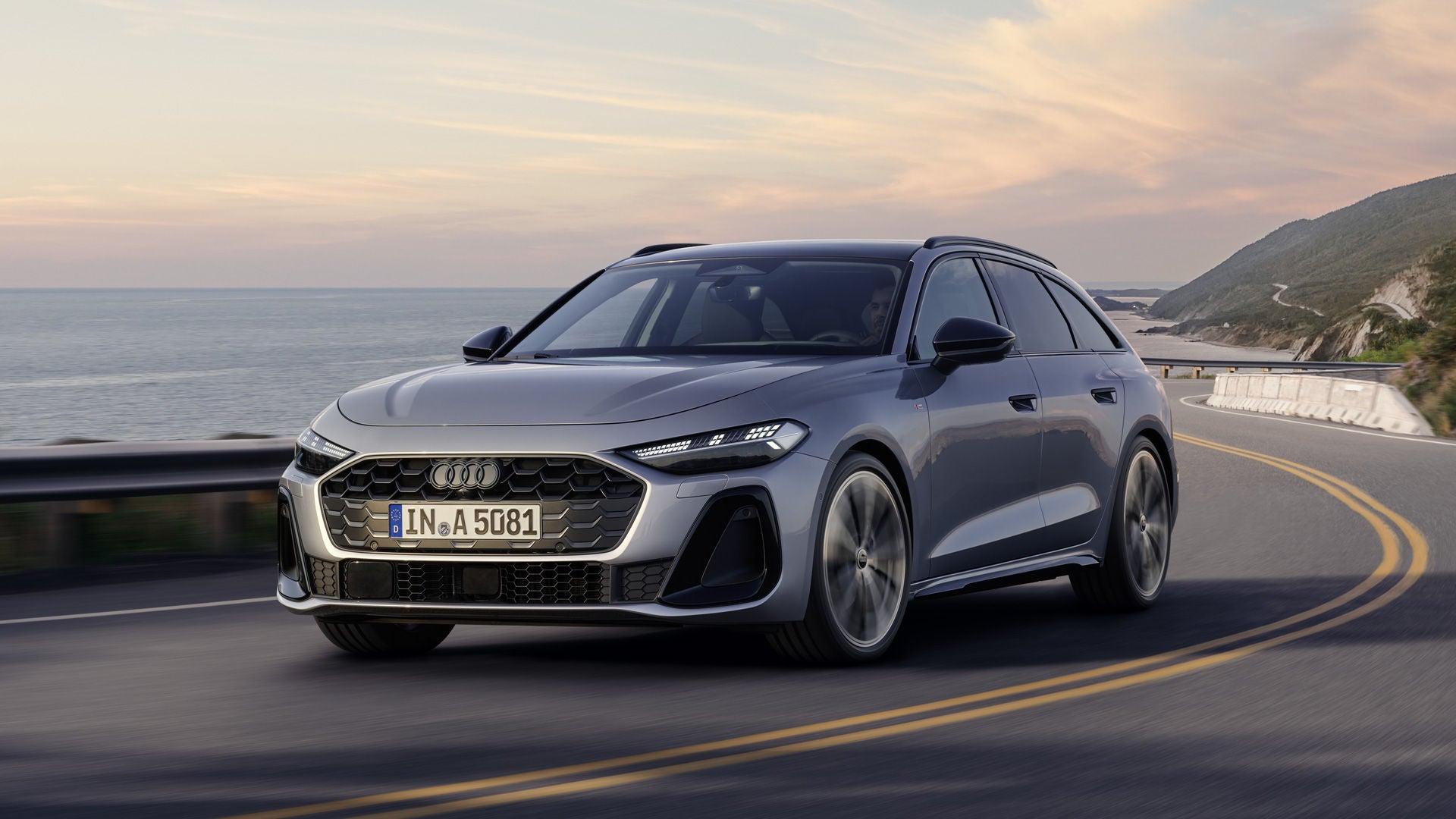 Der A5 Avant in einer schrägen Frontperspektive, während er bei Sonnenuntergang eine kurvige Küstenstraße entlangfährt.