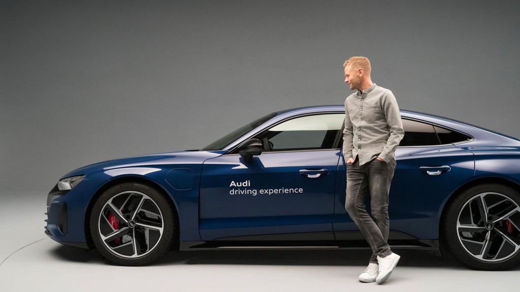Christopher Broeker leaning against an Audi RS e-tron GT bearing the words “Audi driving experience”.