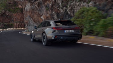 Der Audi A6 allroad e-hybrid schräg von hinten in voller Fahrt auf einer Gebirgsstraße. Rechts ragen steile Felswände auf.
