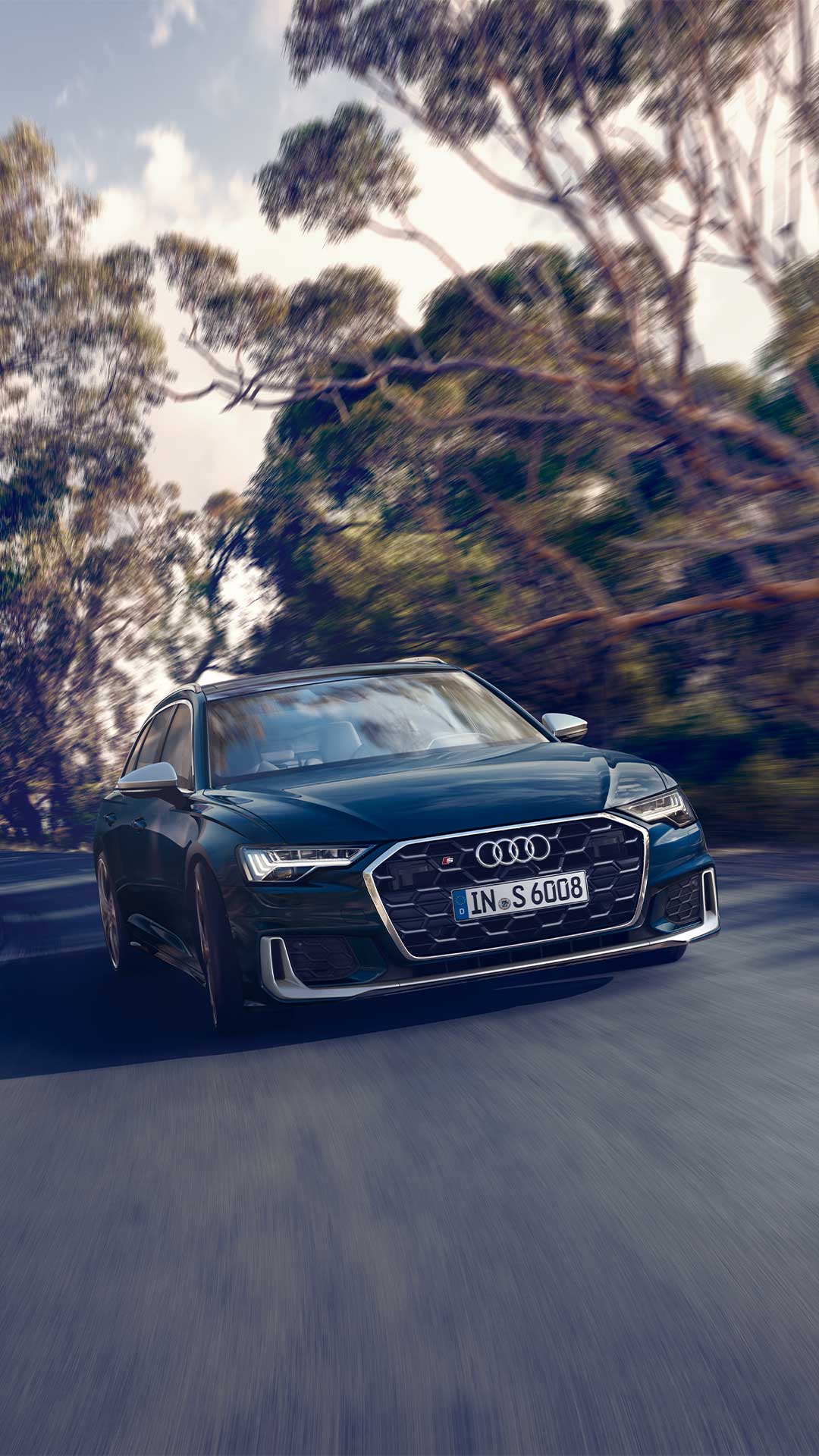 Dunkelblauer Audi S6 Avant TDI fährt auf kurviger Straße durch bewaldete Landschaft, dynamische Bewegung sichtbar.