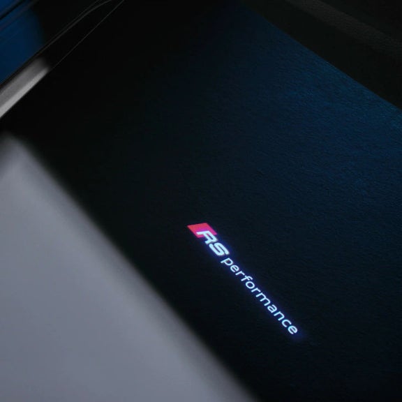 Close-up of an "RS performance" logo illuminated on a textured dark surface.