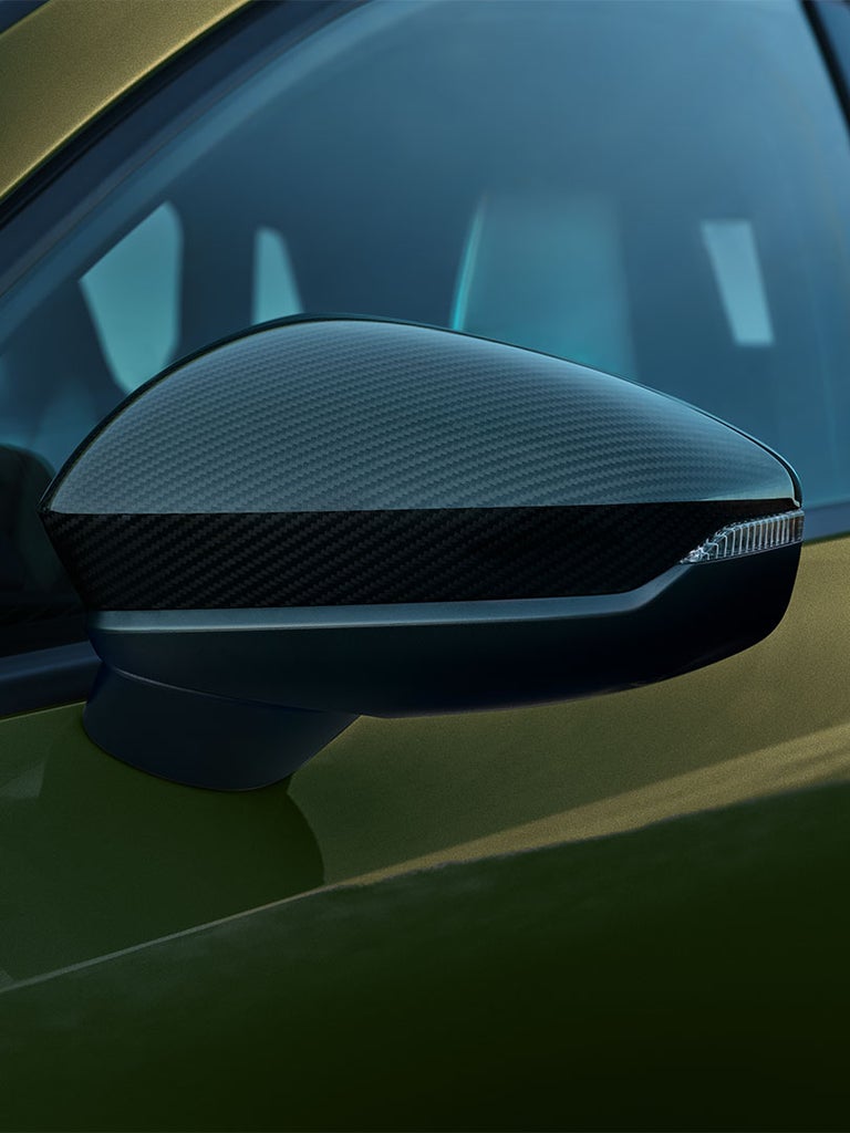 Detailaufnahme eines Außenspiegels in Carbonoptik an einem grünen Audi A3 Sportback vor blau getöntem Fensterhintergrund.
