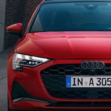 Close-up of a red Audi's front section with a focus on the grille and headlight.