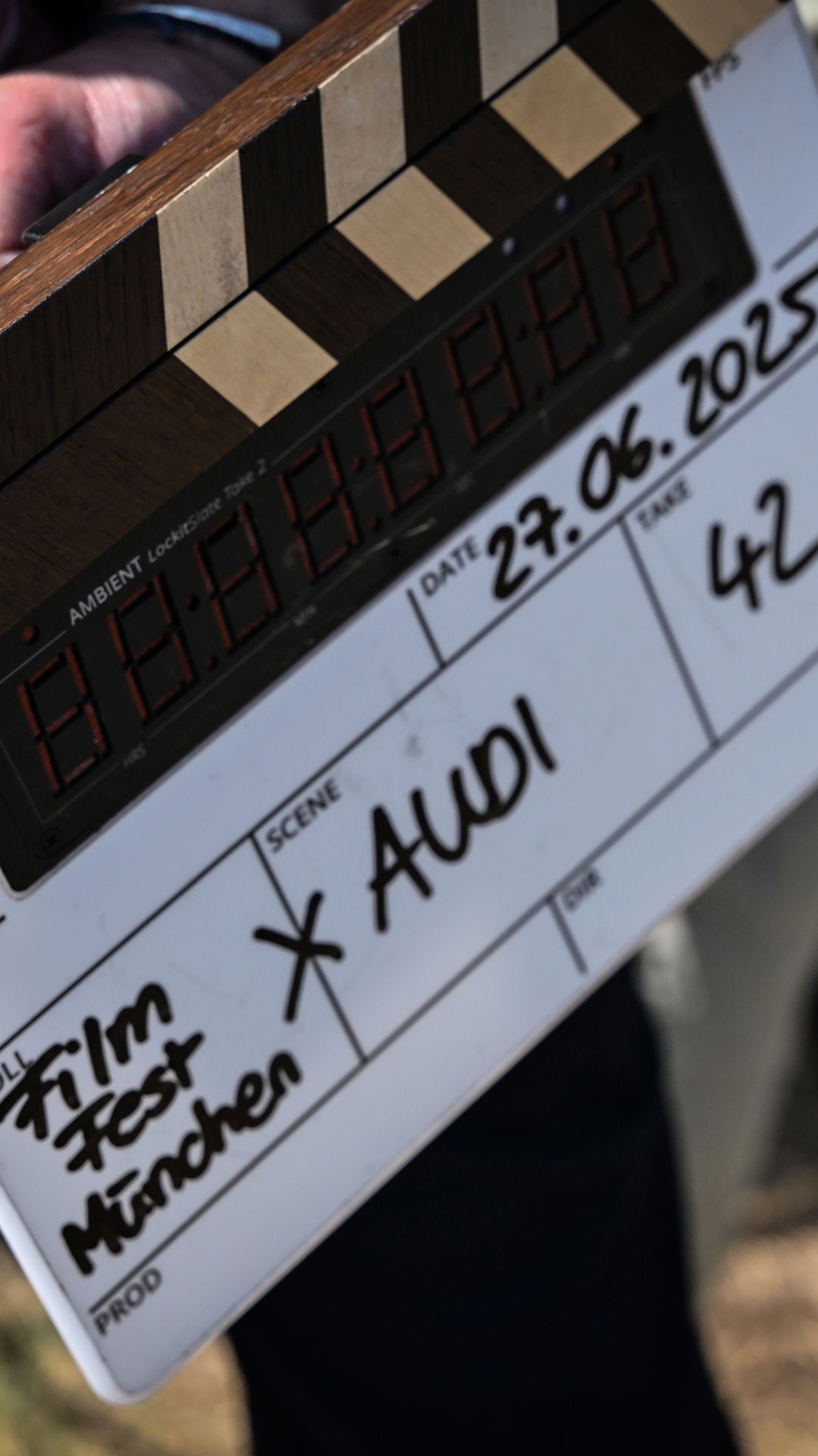 Filmklappe mit handschriftlichem Hinweis „Filmfest München x Audi“ bei einem Außendreh.